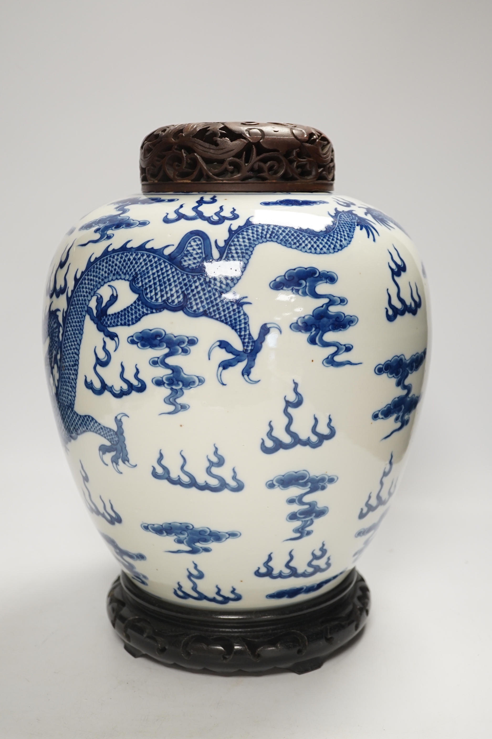 A large Chinese blue and white jar decorated with dragons chasing the flaming pearl together with unassociated carved wood lid and stand, 35cm high